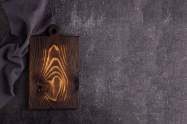 Karanlık bir arka planda eski bir kesme tahtası. Yemek için kesme tahtası. Başlık arkaplanı. Gri keten peçete