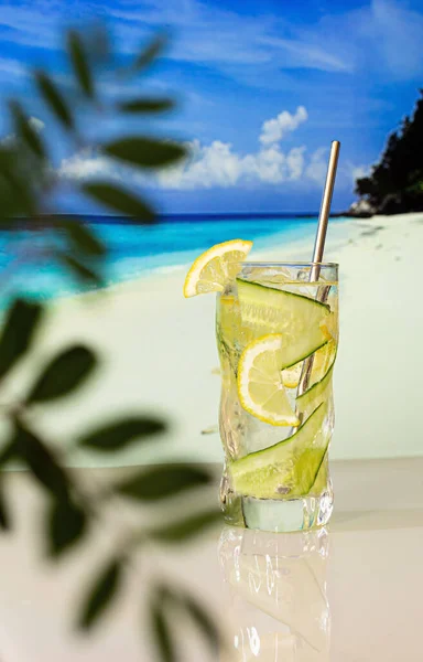Sahilin arka planında limon ve buzlu soğuk kokteyl, mavi deniz ve mavi gökyüzü. Arkaplan camı