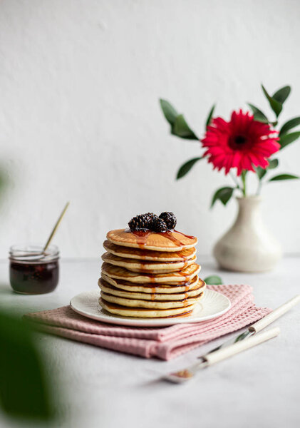 A stack of pancakes with jam from cones on a light background. A plate of pancakes sits on a pink napkin