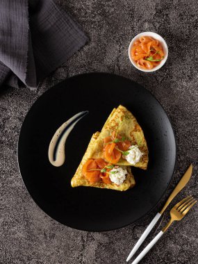 Siyah tabakta somon ve krem peynirli krep. Restoran servisi. Gümüş takımlar ve arka planda gri keten peçete.