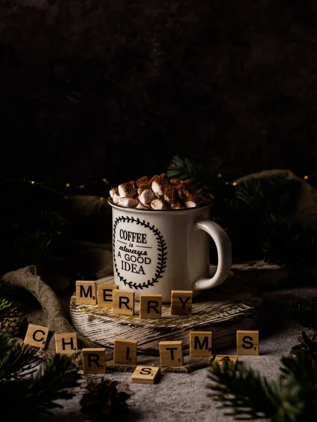 cocoa mug decorated with marshmallows on a dark background. A sprig of spruce, a sieve, a bunch of cinnamon