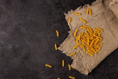 Koyu bir arka planda çuval bezi, üst manzara. Üzerine makarna serpilmiş. Kopyalama alanı