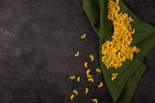 Koyu bir yapısal arka planda izole edilmiş, kopyalayacak bir yığın ham sarı makarna. Makarna manzaralı. Yeşil keten peçetede makarna.