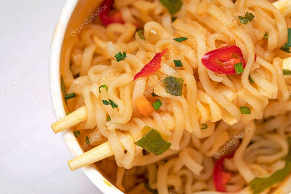 Close-up instant korean ramen noodles soup in a plastic cup with wood chopsticks