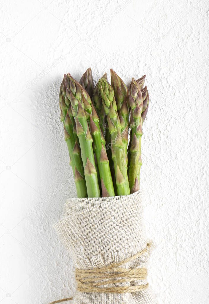 A bundle of a raw green asparagus in a linen cloth on white background, a bunch of a raw asparagus