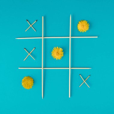 Doğa ateşe karşı. Cyan arkaplanda karahindiba ve kibrit içeren XOX oyunu.