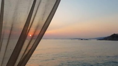 Sahildeki perdenin arkasından gün batımı manzarası. 