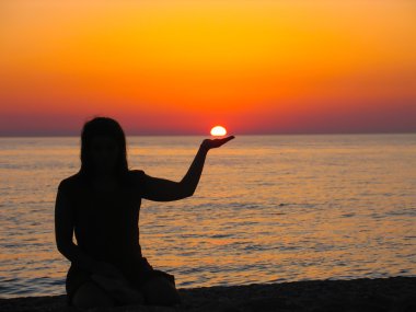 Beautiful sunset with a girl's silhouette holding the sun.