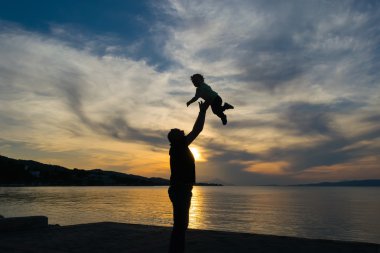 Silhouette of a father and his son against the sunset with a dramatic sky.