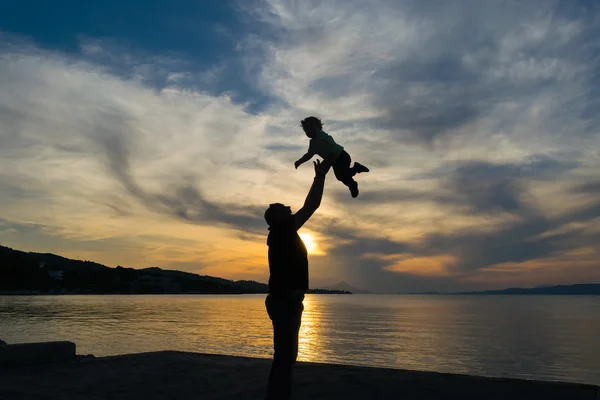 Silhouette eines Vaters und seines Sohnes gegen den Sonnenuntergang mit dramatischem Himmel. — Stockfoto