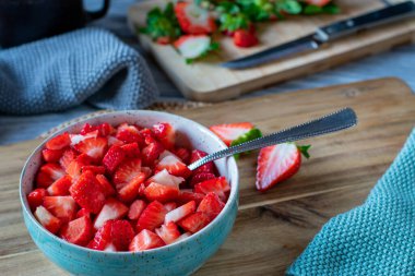 Ahşap kırsal masa arka planında taze doğranmış çilek dolu bir kase. Yukarıdan yakın görünüm