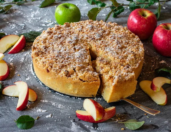 Traditional and rustic german apple crumble cake baked in a round baking pan and served on dark table background with fresh apples.  From above view