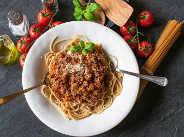 Ev yapımı geleneksel bolonez soslu ve rendelenmiş parmesan peynirli taze pişmiş bir spagetti tabağı. Masa arkasında çatal ve kaşıkla makarna tabağında servis ediliyor. Genel ve yakın görünüm