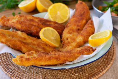 Kırsal bir masada servis edilen taze tavada kızartılmış ve ekmek arası balık filetosu.