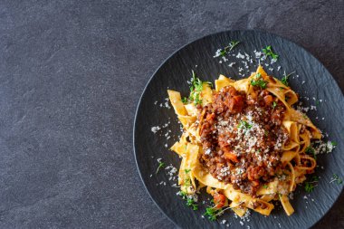 Ev yapımı taze vejetaryen mercimek bolonez sosu makarna ve parmesan peyniri ile servis edilmiş siyah masa arkasında koyu bir tabakta.