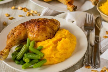 Roasted Chicken legs with potatoe pumpkin puree served with green beans on a plate on dinner table background. 