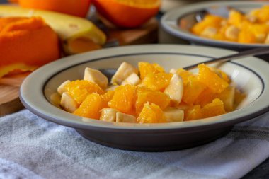 A plate with fresh chopped fruits such as bananas and oranges on rustic table background