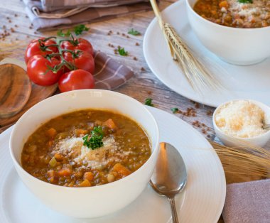 Geleneksel İtalyan mercimek güveci sebzeli pancetta ve rendelenmiş parmesan peyniri ile kaplanmış. Yukarıdan arka planda mutfak masasında beyaz bir kasede servis edilmiş. Yan görünüm