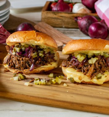 Peynirli sığır burger, karamelize edilmiş kırmızı soğan ve turşu kırsal ahşap kesim tahtasında servis edilir.