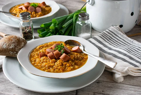 Delicious fresh and homemade cooked vegetables stew made with carrots, potatoes, celery and minced meat served with boiled sausages on a white plate with spoon on kitchen table background