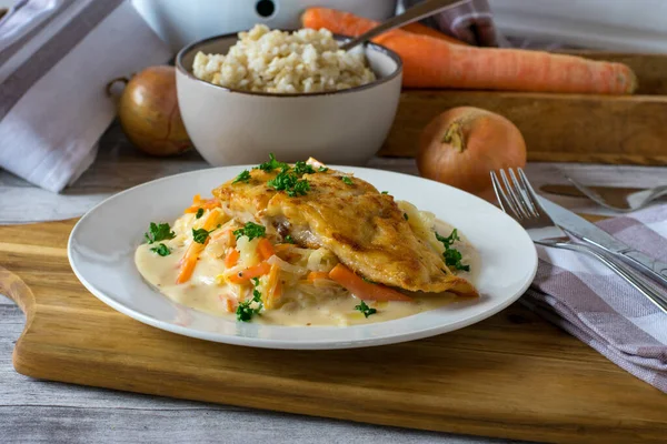home cooked fish dish with floured, pacific salmon fillet served with cabbage and carrot vegetable in a delicious bechamel sauce with brown rice on rustic wooden table background.
