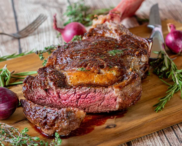 Delicious fresh grilled rib eye steak with bone called tomahawk steak cooked medium rare and served with steak knife and herbs on a wooden cutting board. Quality meat from Ireland