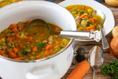 Bezelye ve havuç çorbası patates ve kıyma tenceresinde servis edilen kepçe ve kırsal masa arka planında servis edilen et.