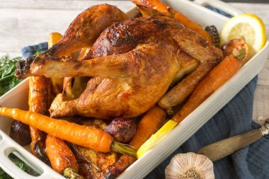 Kızarmış tavuk yemeği ve fırında sebze rustik ahşap masa arka planında güveç tabağında servis edilir.