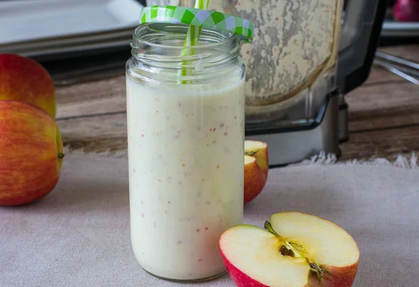 homemade fresh blended drink yogurt with apples served in a glass jar with drinking straw on kitchen table with blender in the background