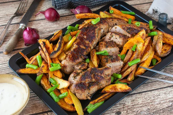 新鲜煮熟的烤箱烤猪肉片 配上土豆和红薯片 与青豆一起放在烤盘上 放在木制烤肉桌上 — 图库照片