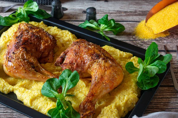 Taze ve ev yapımı fırın ızgara tavuk budu ve kremalı polenta yukarıdan gelen ahşap masa arka planında servis ediliyor.