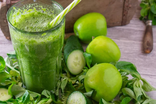fresh blended green smoothie for healthy lifestyle with cucumbers, green apples and lambs lettuce served in a large glass with drinking straw on rustic table background. Closeup and front view