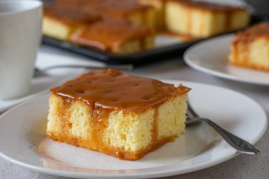 Masada çatalla beyaz bir tabakta servis edilen taze ve ev yapımı karamel kaplı süt keki. Yakın plan ve bulanık arkaplan ile ön görünüm