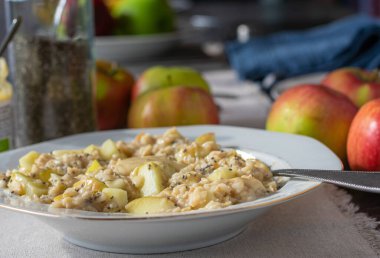 Delicious fresh cooked homemade oat porridge with sauteed apples, chia seeds and almond butter served on a white plate with spoon on kitchen table. Closeup and front view with blurred background