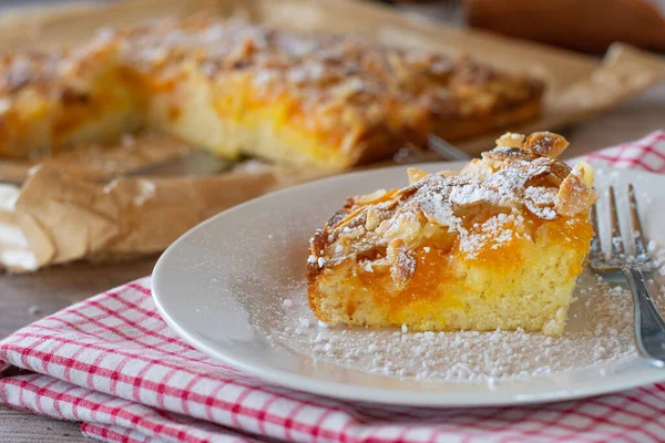 Almond cake with tangerines. A piece of fresh and homemade baked almond cake with tangerines served on a white plate with fork on rustic table background. Closeup