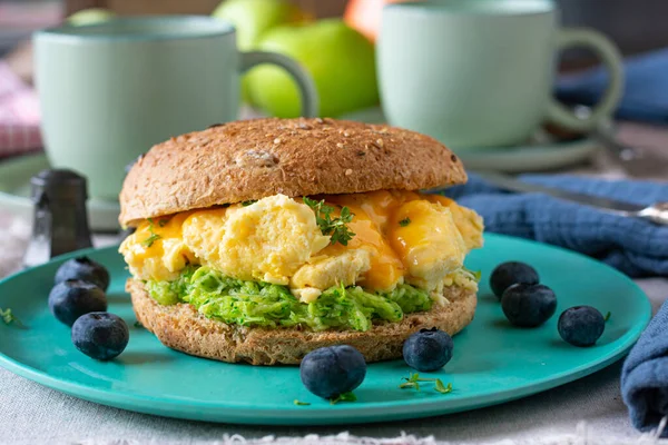 Delicious vegetarian and clean eating breakfast or lunch burger sandwich with scrambled eggs, cheese and glazed zucchini served on a climate friendly bamboo plate on kitchen table background