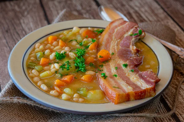 新鲜而自制的白豆汤 配以根蔬菜和猪肚 用勺子和木桌底盘 闭包视图 — 图库照片