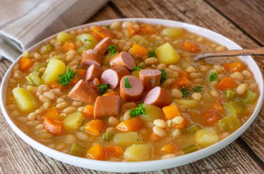 Sebzeli fasulye çorbası. Taze ve ev yapımı çorba ya da fasulyeli güveç, haşlanmış sosis, sebze ve patates bir tabak ya da kırsal ve ahşap masa zemininde kaşıkla servis edilir.