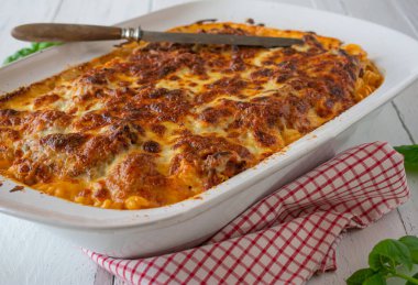 Makarna güveci. Ev yapımı İtalyan mutfağı. Taze bolonez soslu erişte güveci ve mozzarella peyniri ile kaplanmış beşamel sosu beyaz ahşap masada bir fırın tabağında servis ediliyor. Yaklaş ve izole edilmiş görünüm
