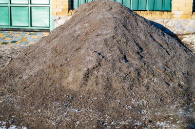 Kışın güneş ışığı altında evin yakınındaki kum yığını. Kaliteli bir fotoğraf. Konut binasının yanında büyük bir kum yığını. Ev yapımı, inşaat malzemeleri ve mevsimlik açık hava çalışmalarını temsil ediyor..