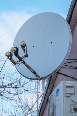 Kışın konut binasında buz saçakları olan büyük bir uydu anteni. Yüksek kalite fotoğraf. Donmuş bir uydu çanağının geniş görünümü, birden fazla LNB kafası ve duvarında uzun buz saçakları olan ev iletişim sistemleri üzerindeki kış havası etkilerini vurguluyor..