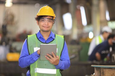 Güvenlik başlığı ve yansıtıcı bez içinde Asyalı mühendislik yöneticisi dijital tablet kullanarak fabrikanın içini kontrol ediyor.