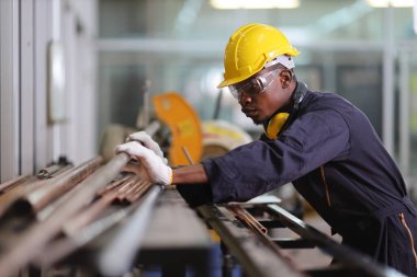 Afro-Amerikan makine mühendisi, fotokopi alanı olan soğutucu fabrikasında çalışırken testere kesmek için bakır tüpü seçiyor.