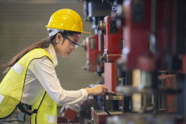 Güvenlik kaskı ve yansıtıcı bez giyen Asyalı kadın tamirci fabrikanın içinde torna makinesiyle çalışıyor.