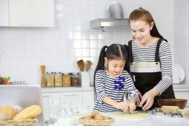 Mutlu Asyalı anne, genç kızına beyaz modern mutfakta hamurdan ekmek yapmayı öğretirken aynı zamanda kurabiye kalıbı kullanıyor.