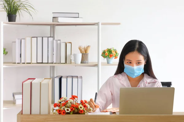 Female employee wearing medical facial mask working from home as social distancing policy in the business office during new normal change after coronavirus or post covid-19 with copy space