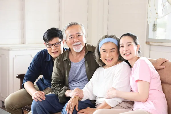 Yaşlı aileleri ve iki orta yaşlı çocuğu olan Asyalı bir aile birlikte oturma odasında rahat bir kanepe üzerinde emeklilik ve mutlu bir yaşam konsepti için oturuyorlar.