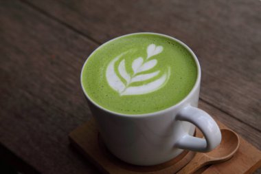 Bir fincan sıcak Japon kibrit yeşil sütlü latte. Lale desenli. Kırsal koyu ahşap masa üzerinde.