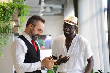 Resmi giyinmiş Kafkas işadamı ve lüks tropikal otel lobisindeki Afrikalı Amerikalı arkadaşı