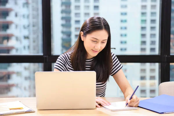 Young Asian student  studying online class from internet sitting in the modern cafe and co-working space with skyscraper view